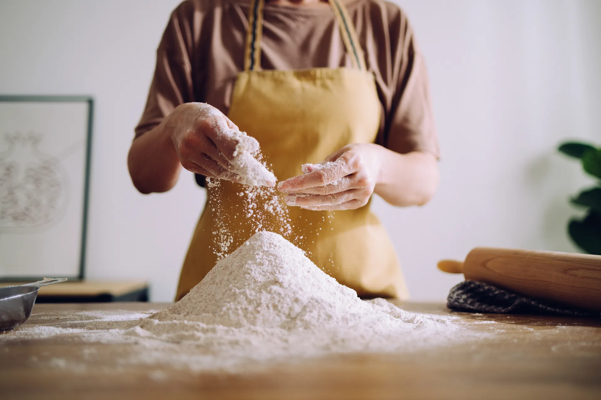 Hands sifting flour over a wooden table in a home kitchen