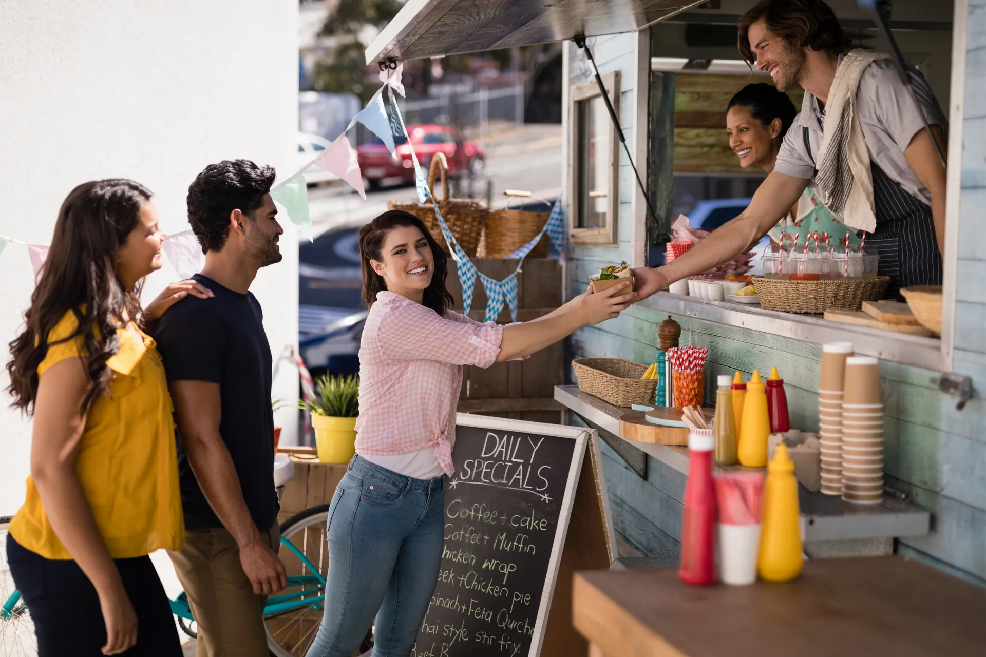 A customer smiling as she's handed her order at a food truck window while friends wait behind her